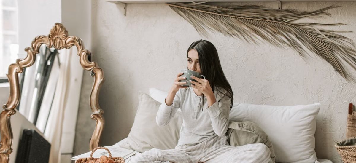 Woman in pajamas enjoys coffee and pastries in a stylish and cozy bedroom setting.