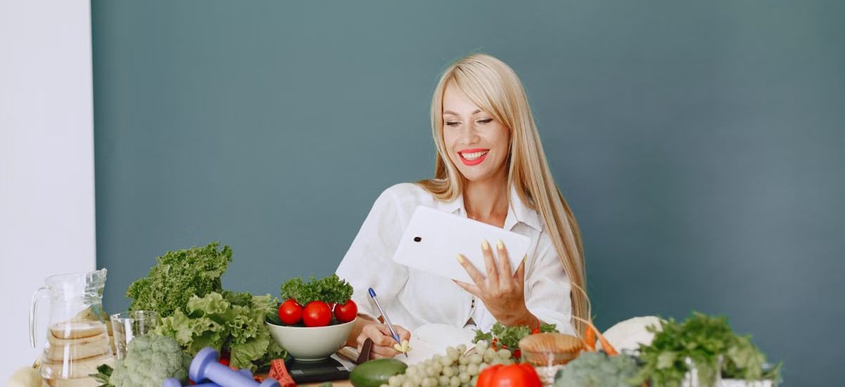 Woman using a tablet surrounded by fresh vegetables at a table, showcasing healthy lifestyle and technology.